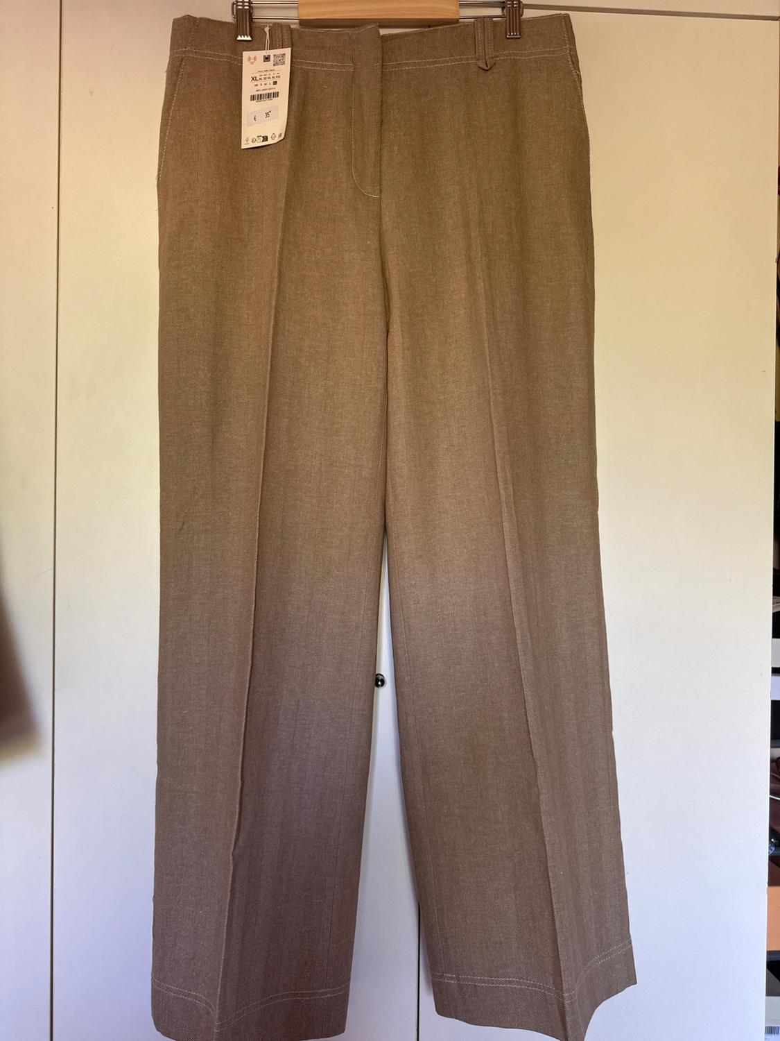 Brown fabric trousers hanging on a coat hanger with visible label. White background.