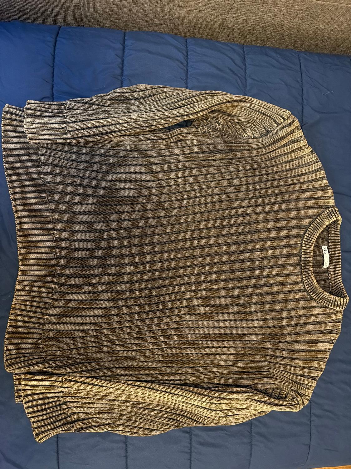 Ribbed knit jumper in shades of brown and grey, placed on a blue quilt. Label visible on the collar.