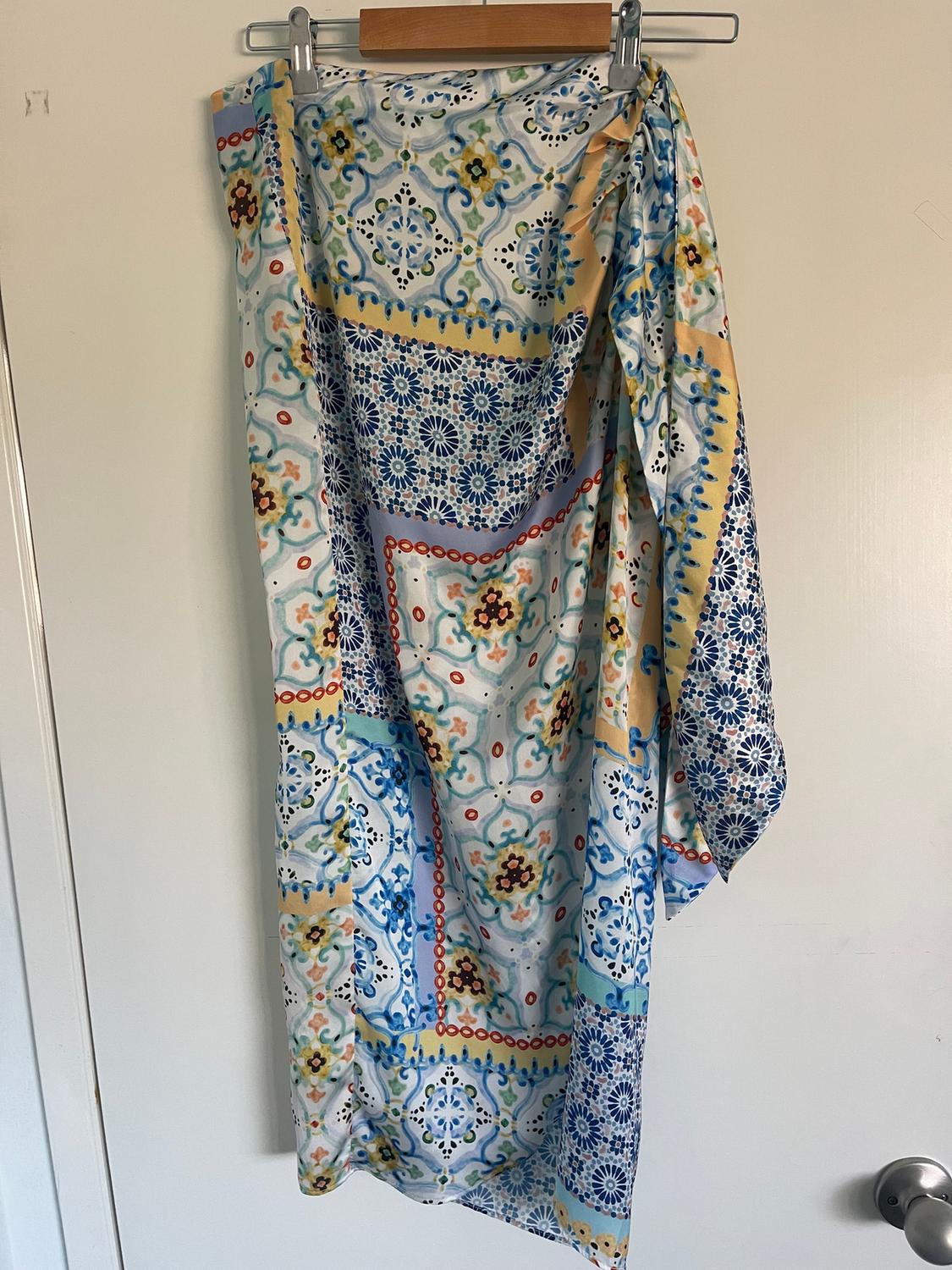 Fabric hung with a mosaic print in shades of blue, yellow, and red, on a wooden hanger on a white door.