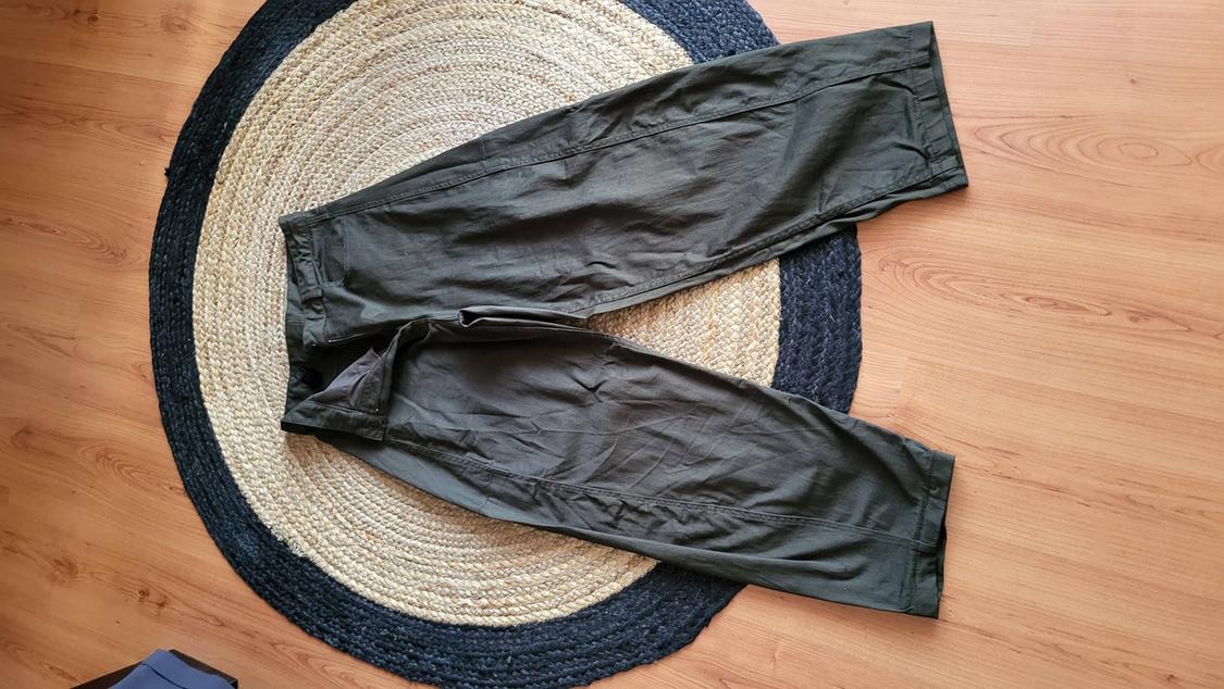 Green, light-fabric trousers placed on a round jute rug on a light wooden floor.
