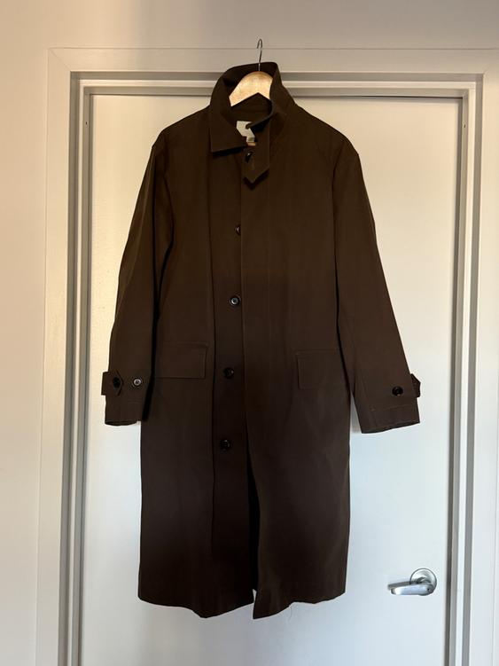 Brown coat hanging on a white door, with dark buttons and front pockets. Interior setting with soft lighting.