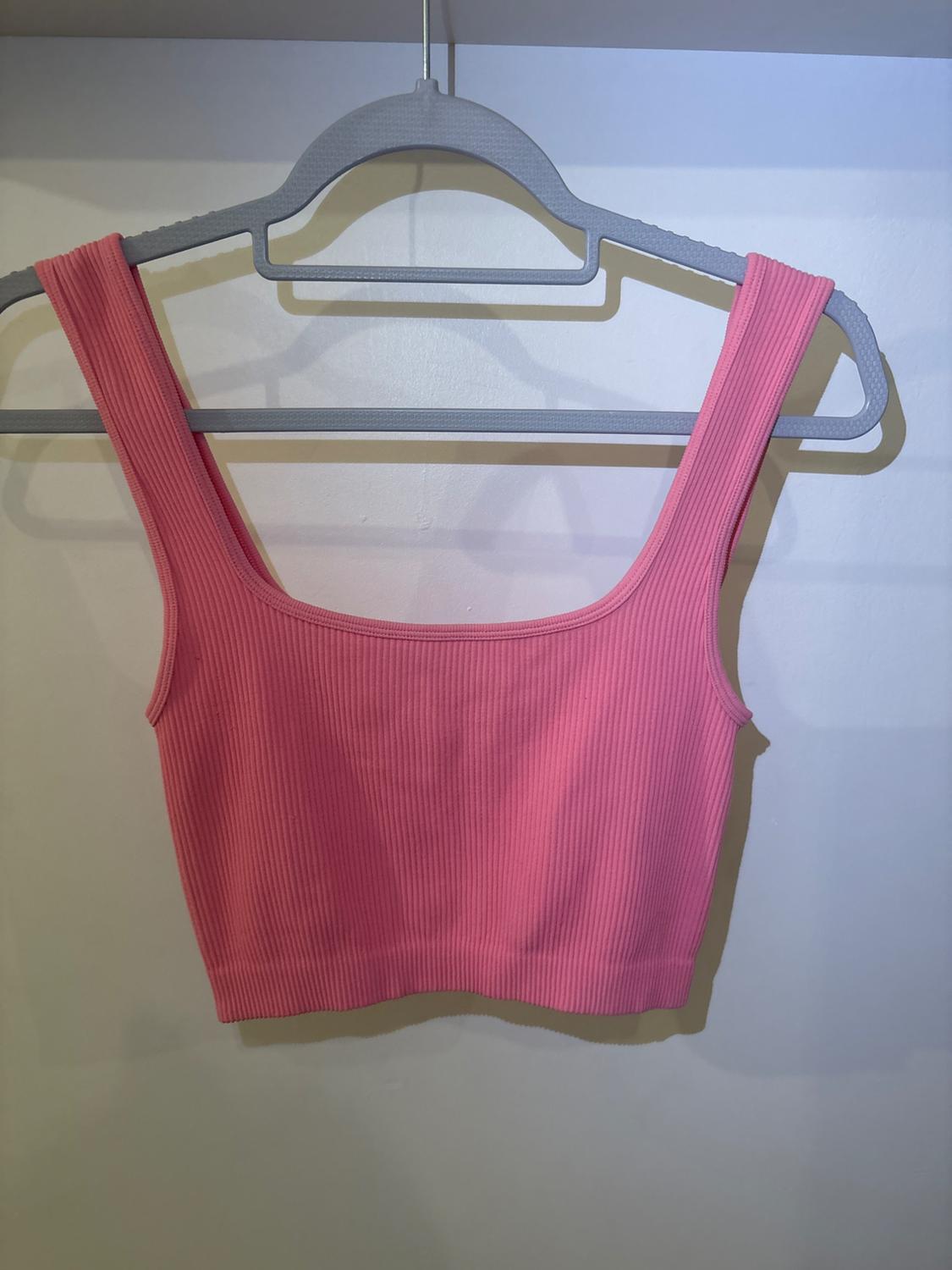 Pink ribbed crop top with wide straps, hanging on a grey hanger against a white background.