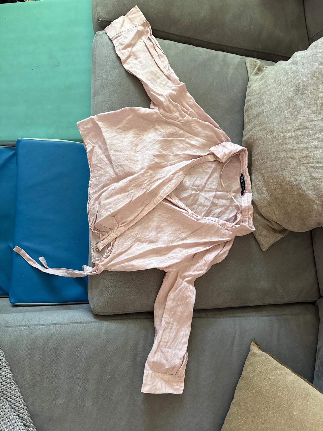 Light pink long-sleeved shirt with a bow, spread out on a gray sofa with beige and blue cushions.