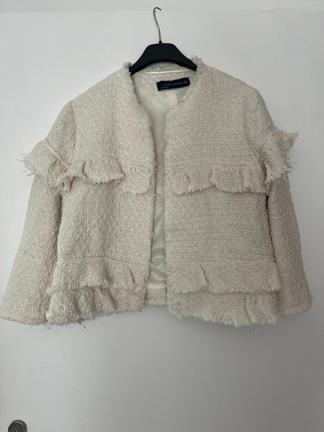 Front view of a beige jacket with ruffles and a woven texture.
