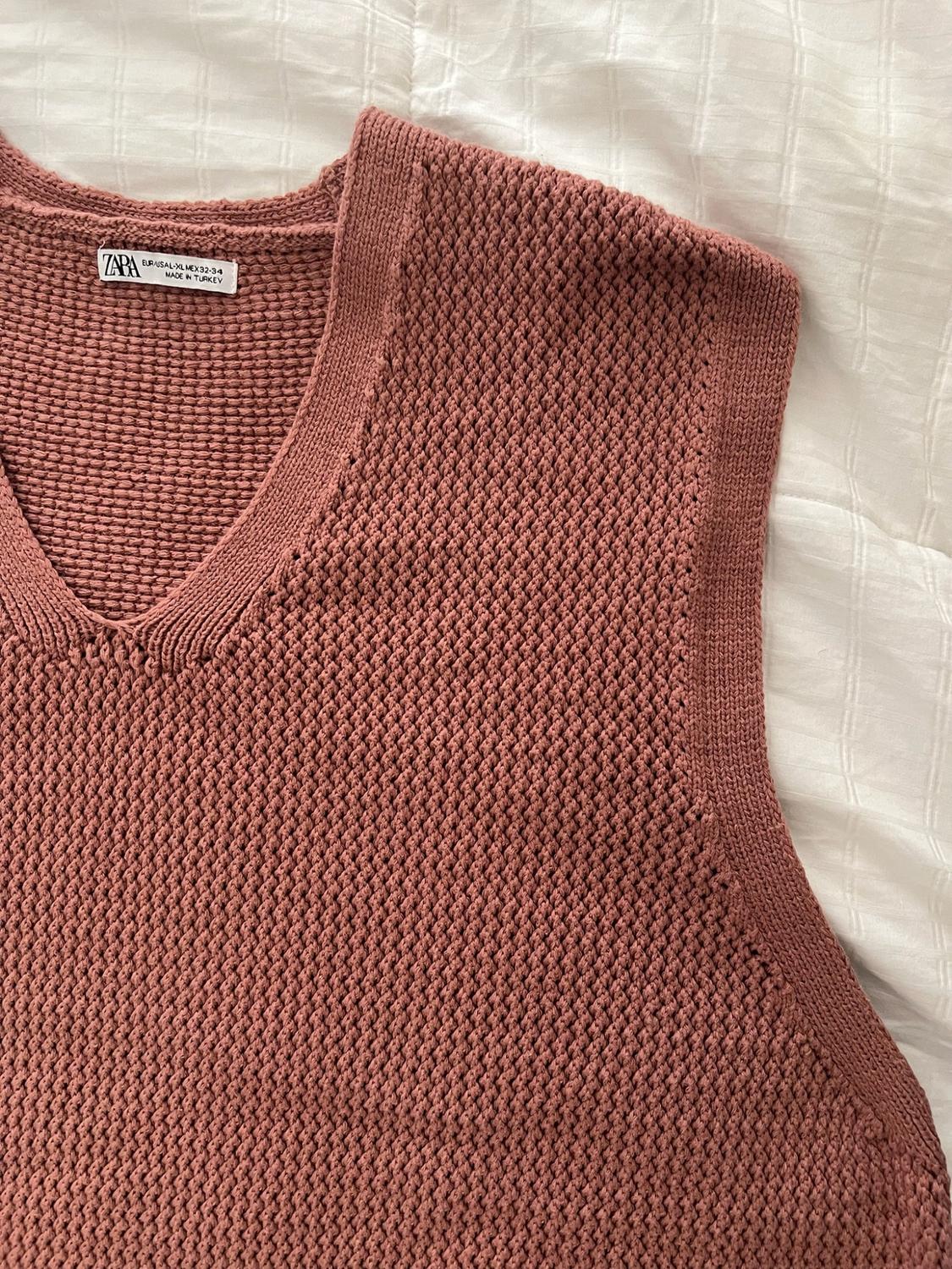 Pink knit vest with a V-neck over white fabric. Text: ZARA EUR/USA L-XL MEX 42-44 MADE IN TURKEY.
