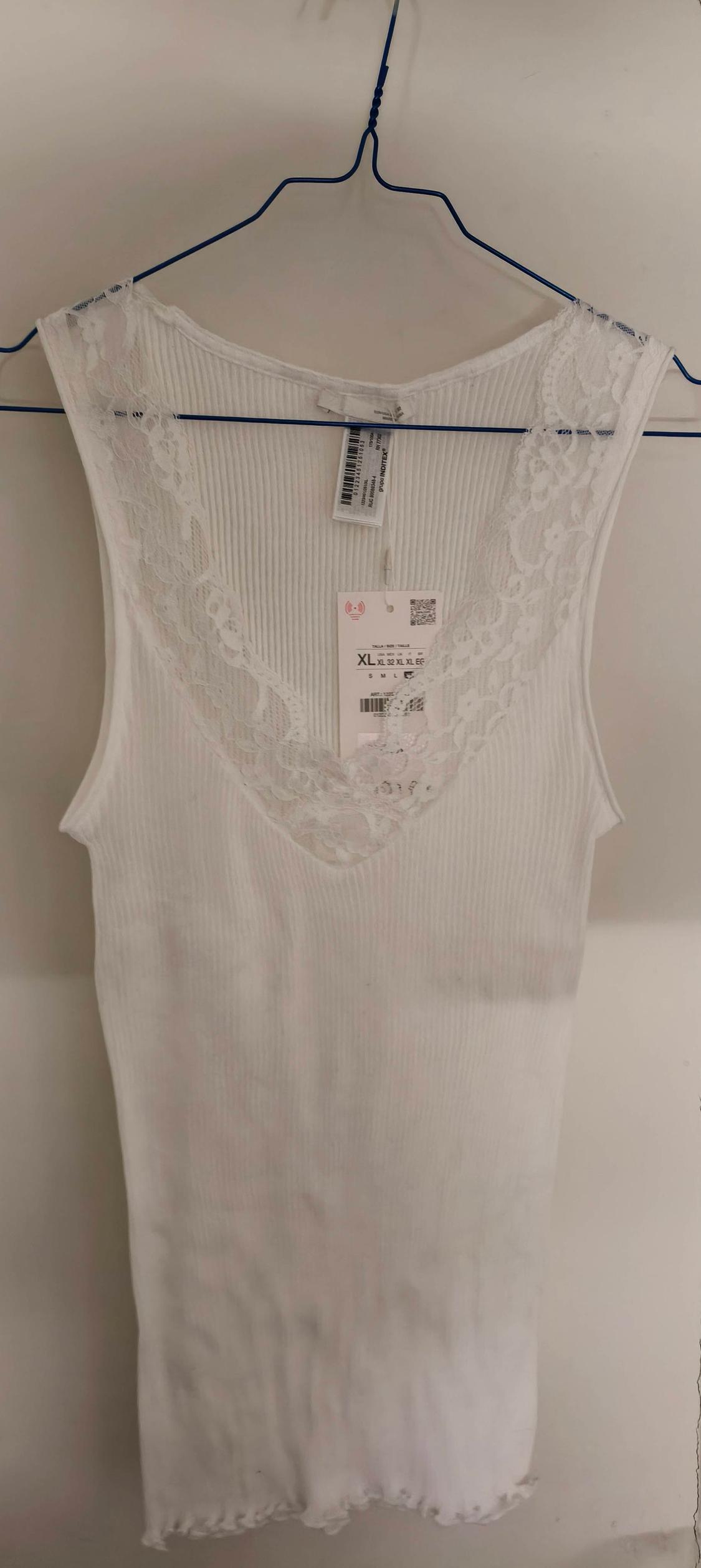 White vest top with lace trim on the neckline, hanging on a blue hanger. Visible label with size XL.