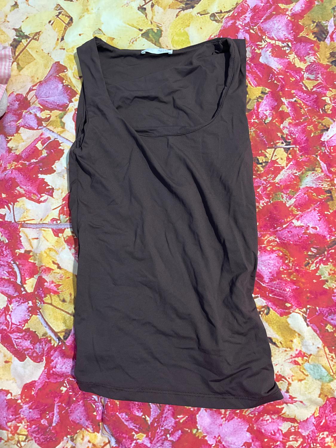 Black sleeveless top on a floral bedspread in shades of red, yellow, and pink.