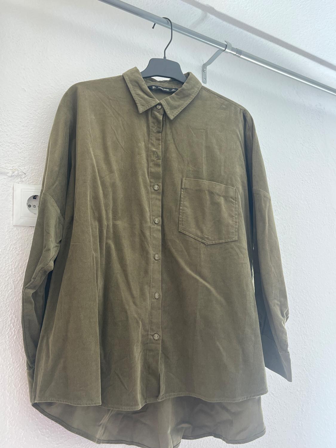 Olive green long-sleeved shirt hanging on a black hanger, with a chest pocket and front buttons, on a white background.