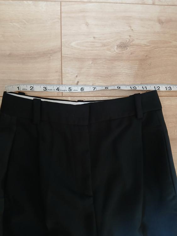 Black trousers on a light wooden floor with a tape measure on top, showing measurements in inches and centimetres.