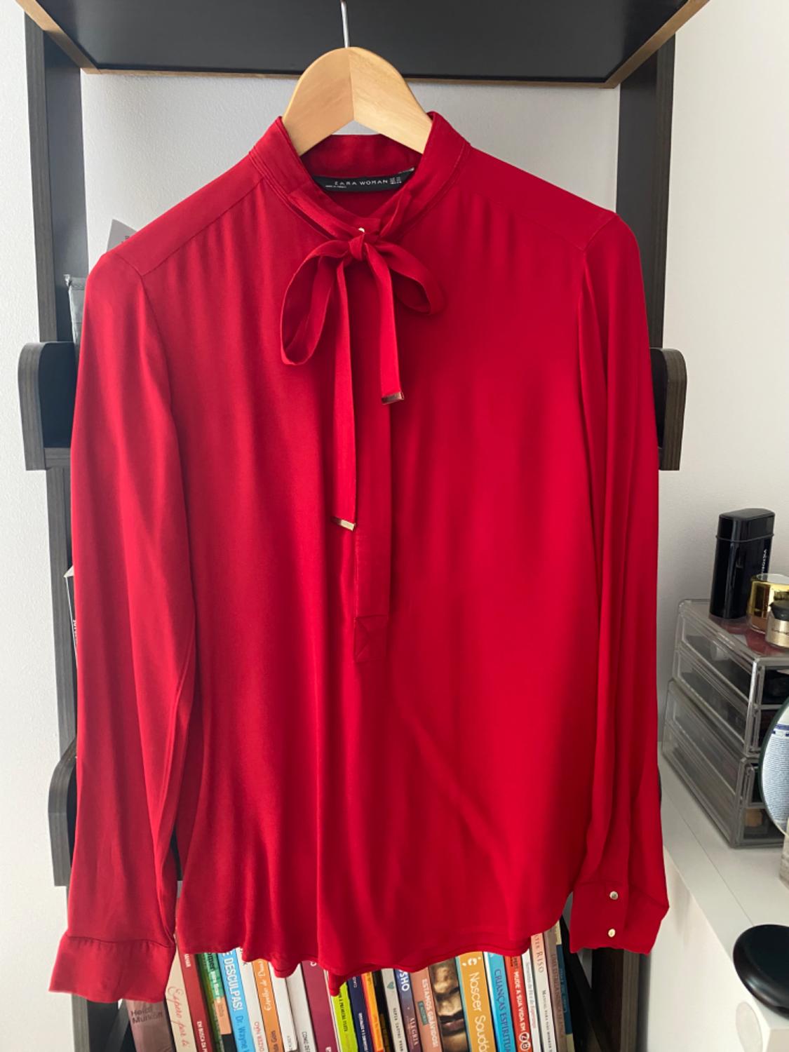 Front view of a red blouse with a tie neck and long sleeves.