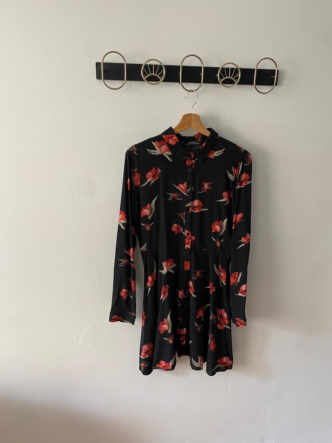 Μαύρο φόρεμα με κόκκινο floral print κρεμασμένο σε ξύλινη κρεμάστρα πάνω σε διακοσμητικό γάντζο στον λευκό τοίχο.
