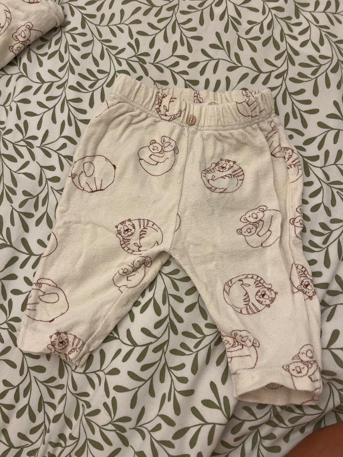 Children's beige trousers with an animal print in brown tones, on a bed with a green leaf patterned sheet.