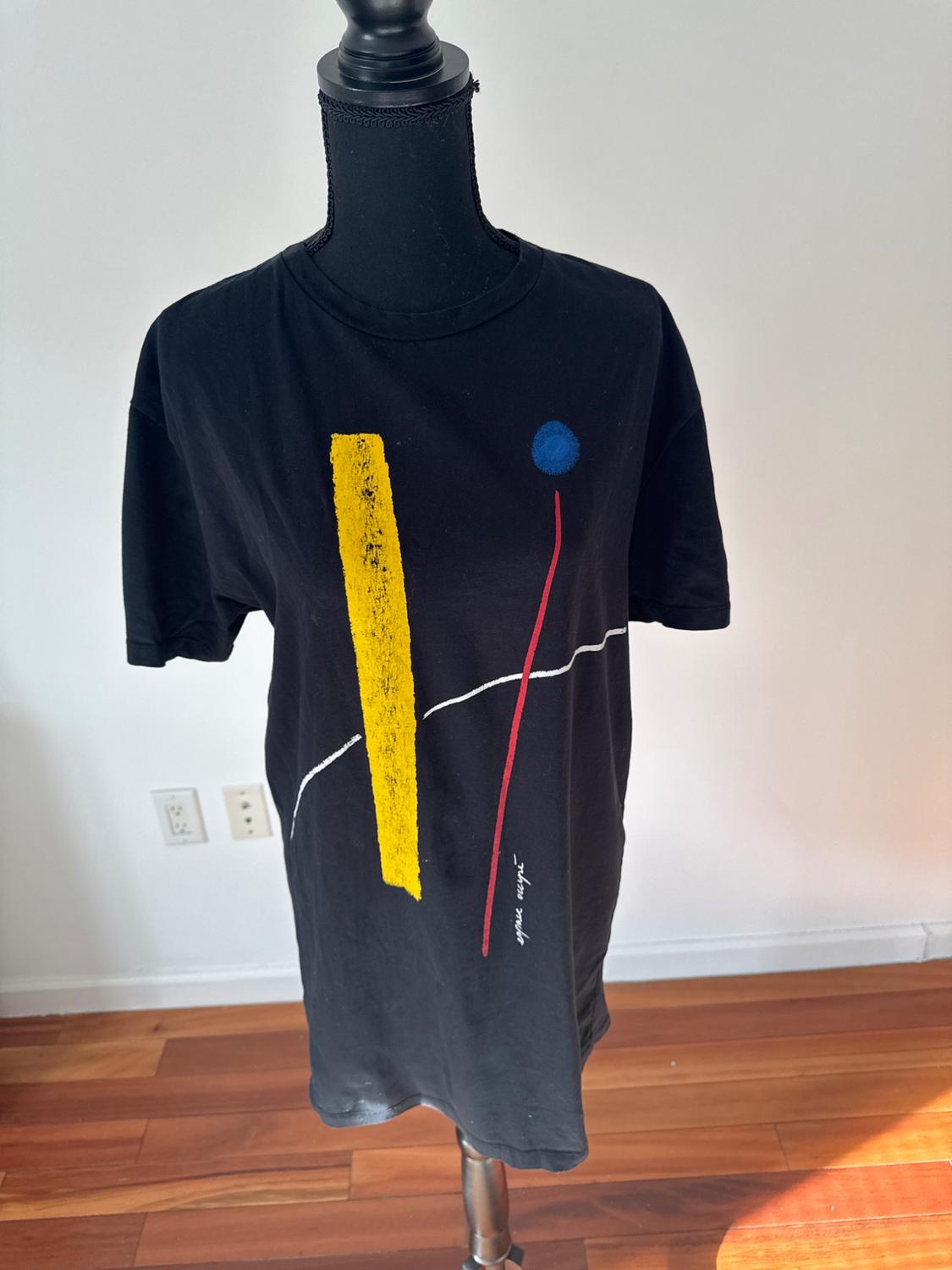 Front view of a black t-shirt with an abstract print in yellow, blue, and red with illegible text.