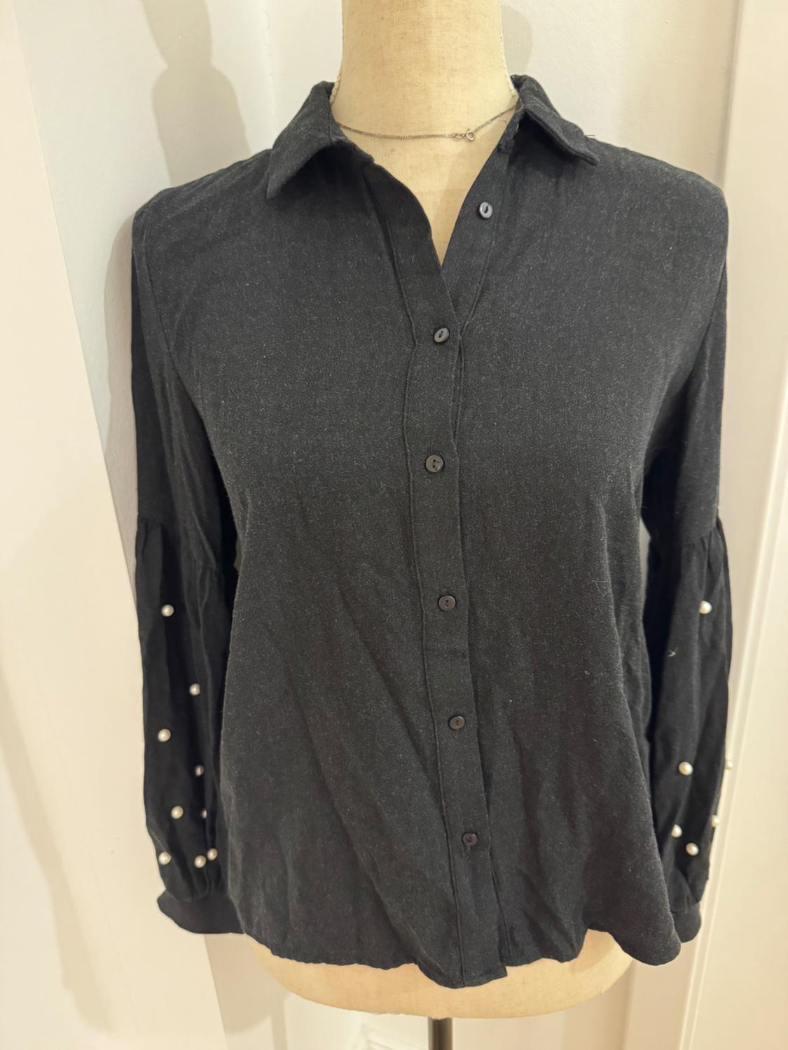 Mannequin in a black button-up shirt, classic collar, and long sleeves decorated with pearls. White background.