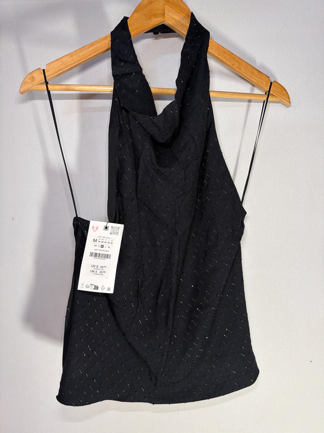 Black top with glitter details hanging on a wooden hanger. Visible tag with price: US$ 45, UK£ 25.