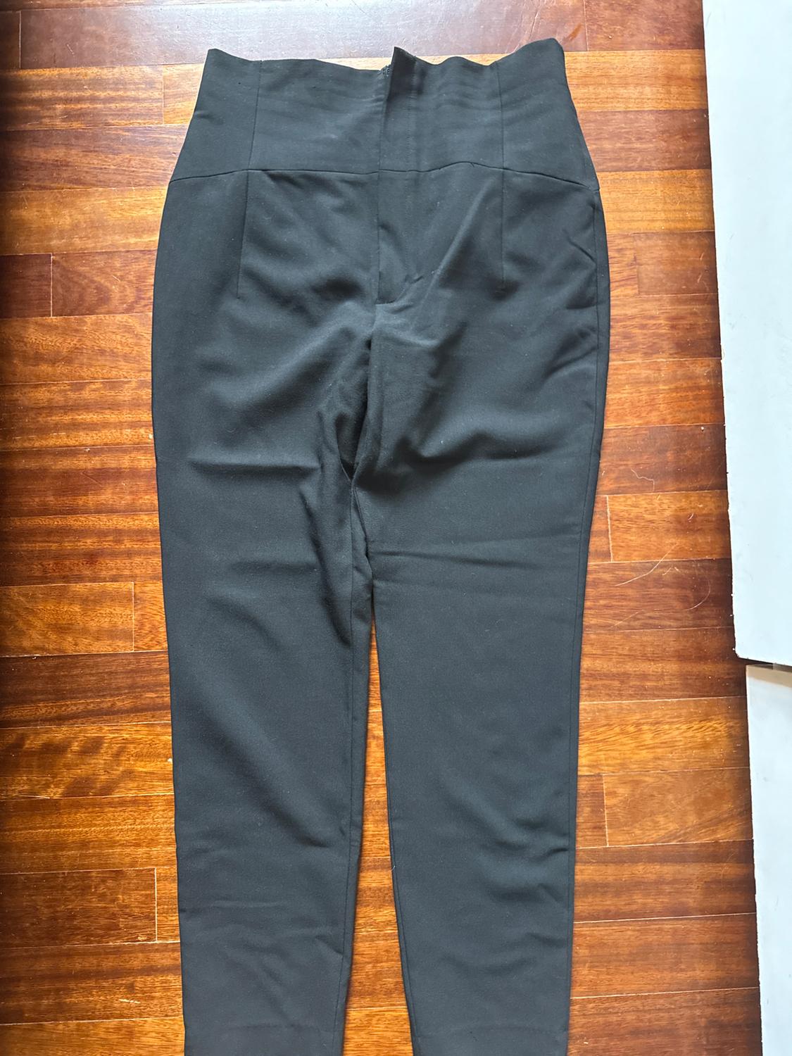 Black high-waisted trousers on a brown wooden floor. The fabric appears smooth and the design is simple and elegant.