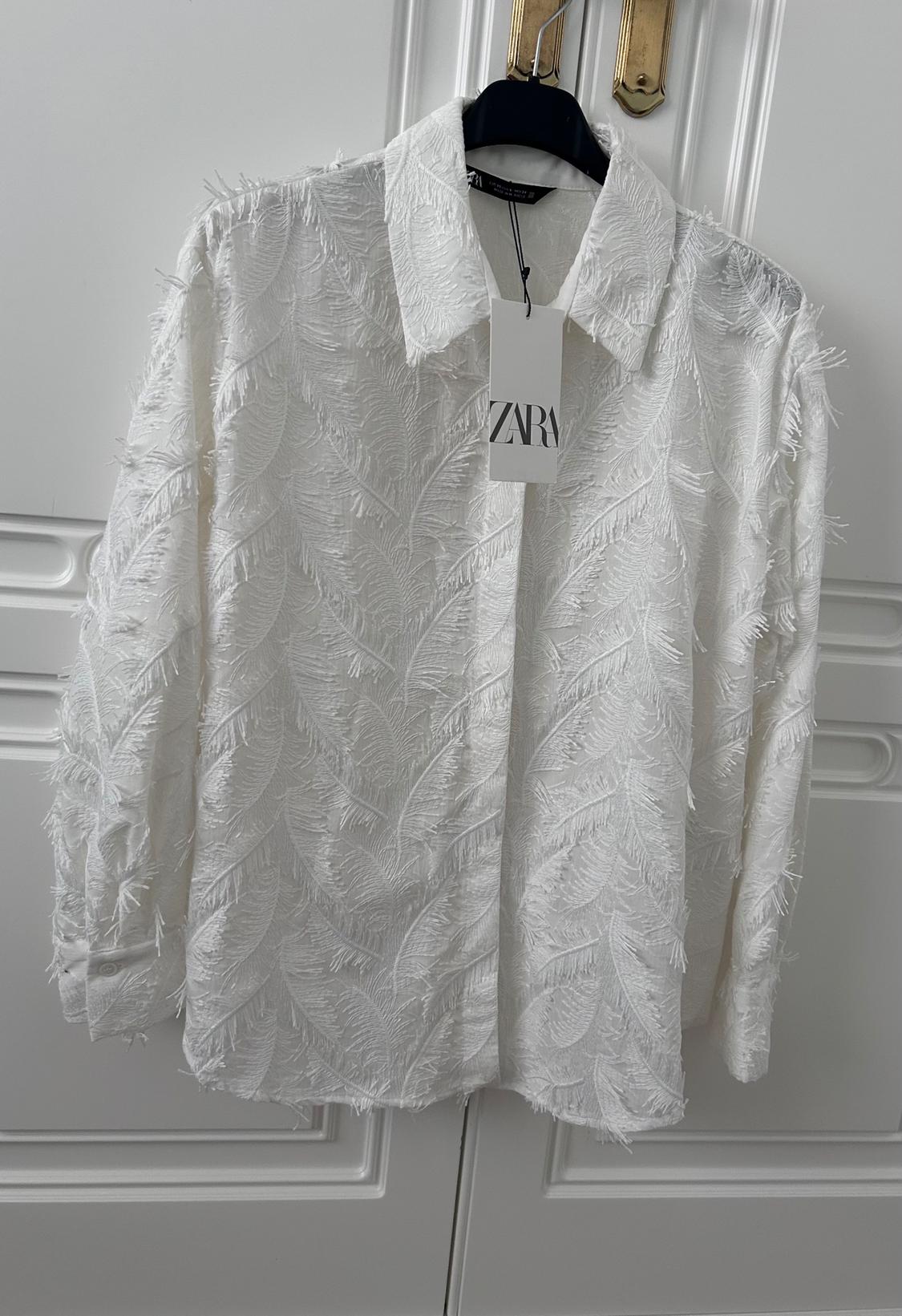 White shirt with leaf texture hanging on a black hanger. Label with the text "ZARA" visible on the front.