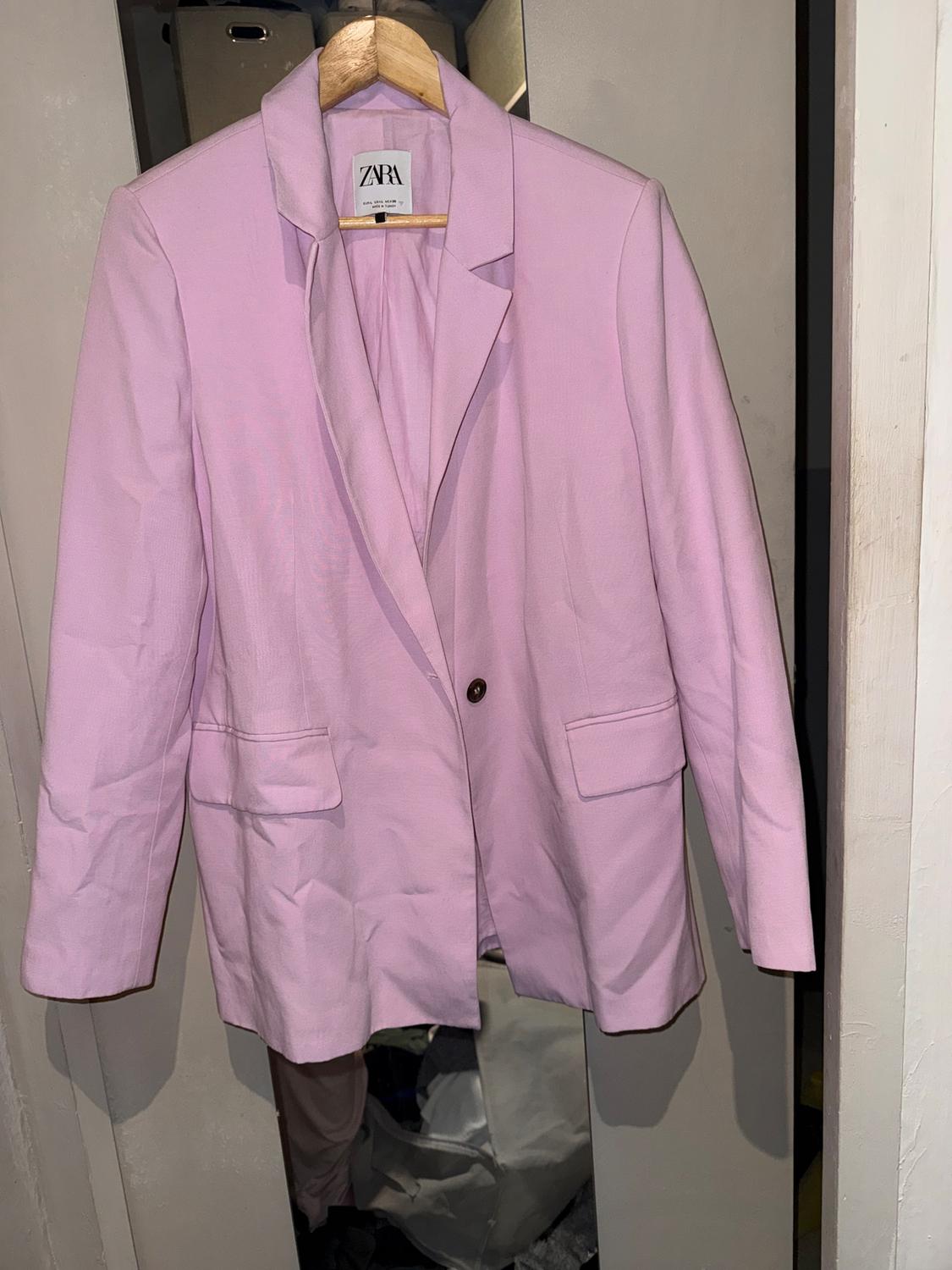 Light pink jacket hanging on a wooden hanger, with a visible Zara tag, in an open wardrobe.