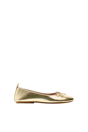 Metallic gold flat ballet pump with a bow on the toe and a heel tab, side view on a white background.