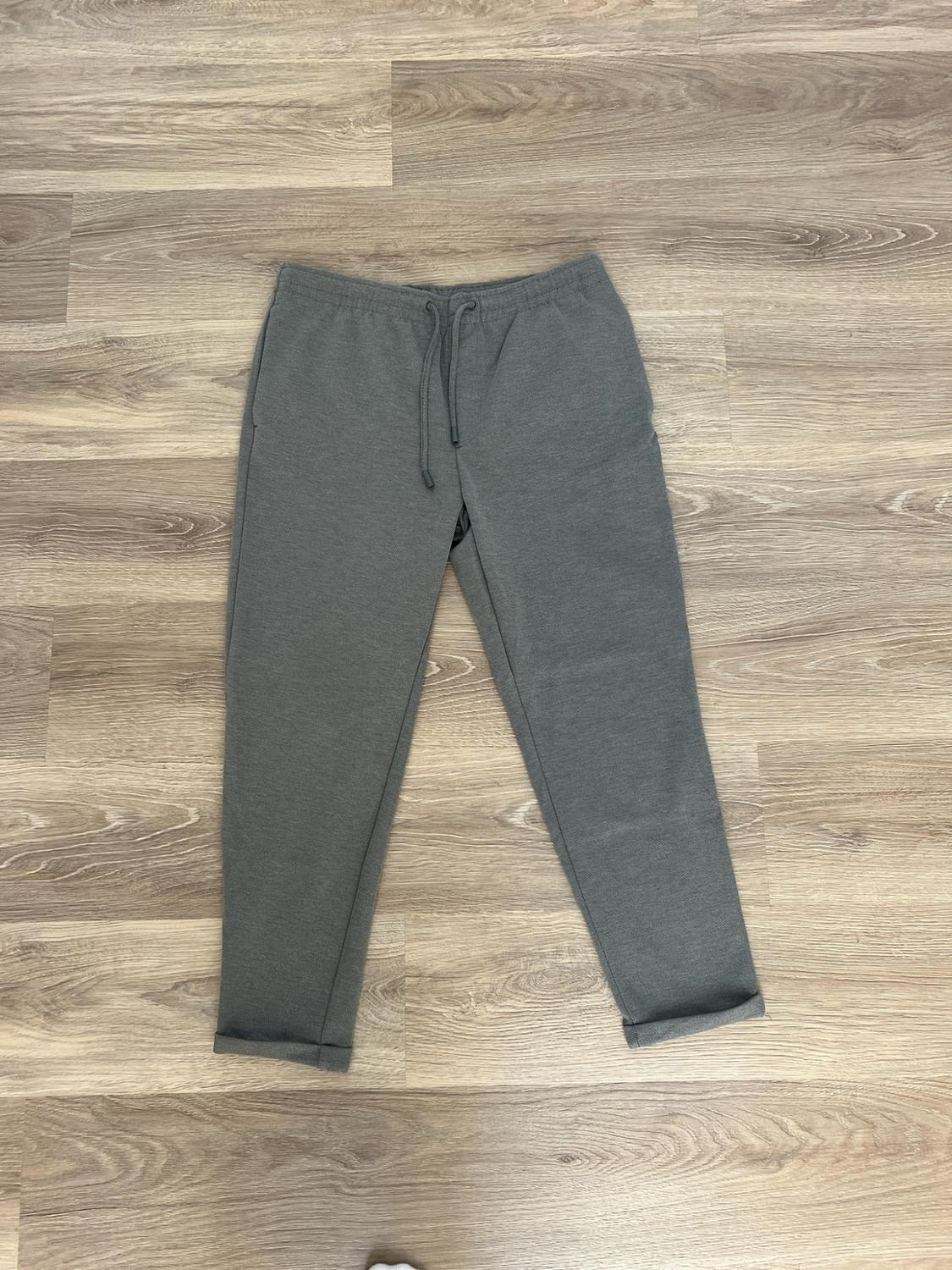 Grey tracksuit bottoms with a drawstring waist and cuffed hems, laid on a wooden floor.