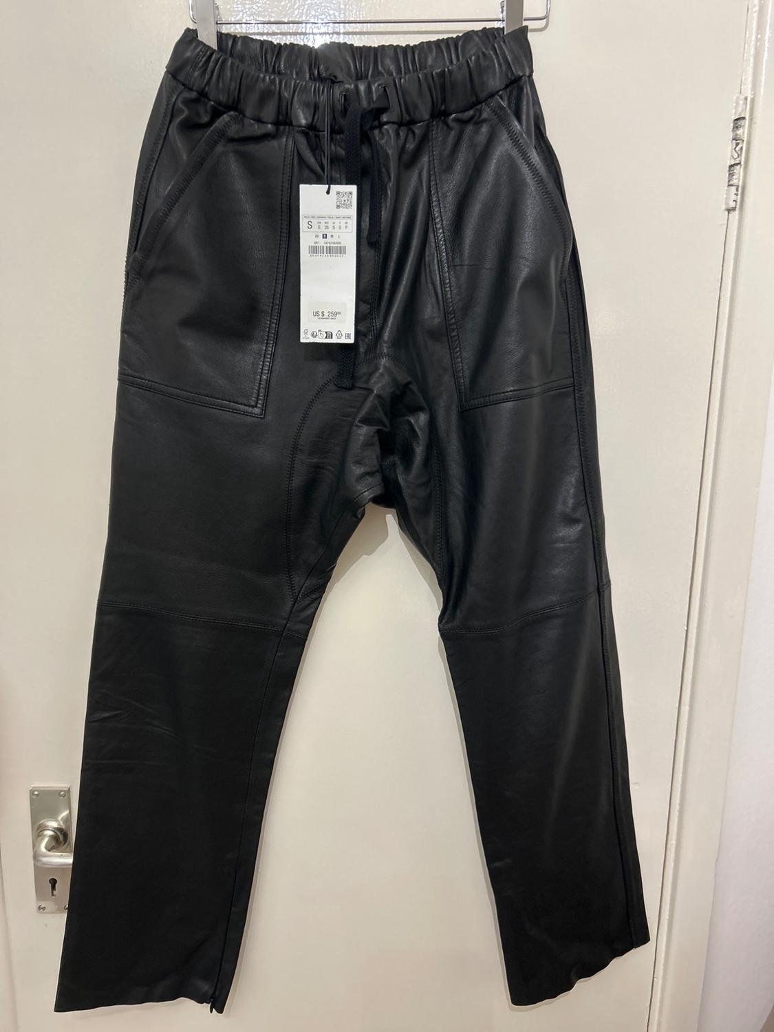 Black trousers hanging on a hanger with a visible tag showing size S and a price of $29.99, over a white door.