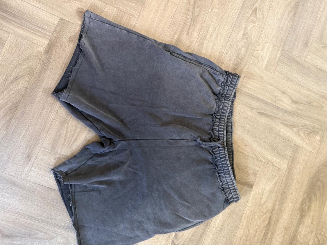 Dark grey jersey shorts with an elasticated waistband and raw hem, laid out on a light herringbone wood floor.