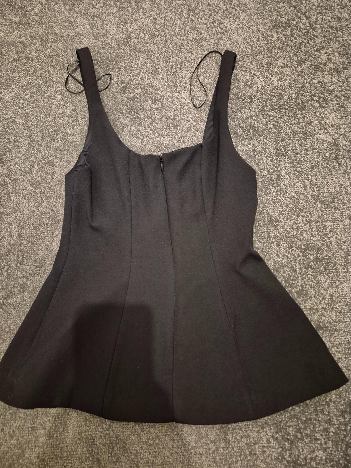Black sleeveless top with thin straps, back fastening and flared design, on a grey rug.