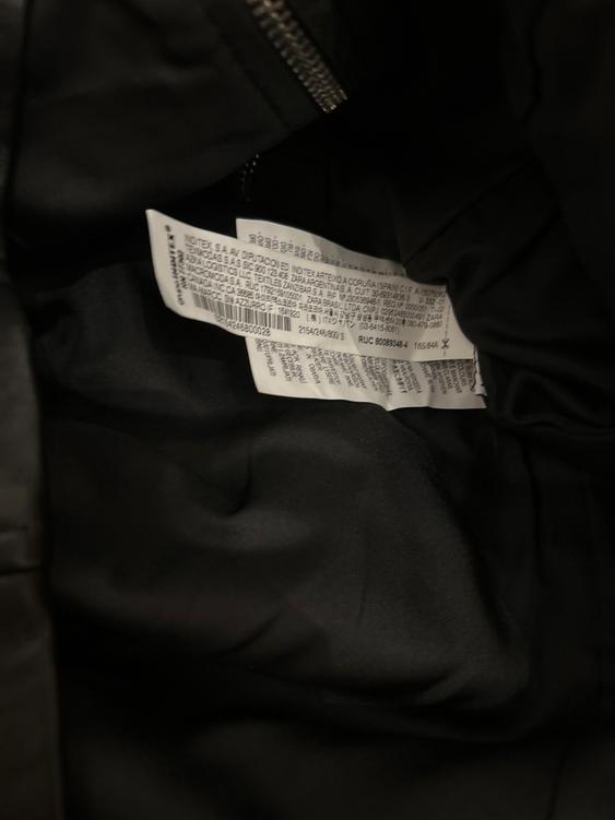 White label with black text inside a black garment, a metal fastening visible in the top left.