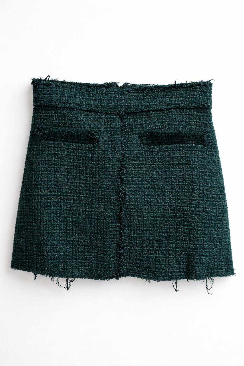 Dark green textured fabric miniskirt with frayed edges and decorative front pockets.