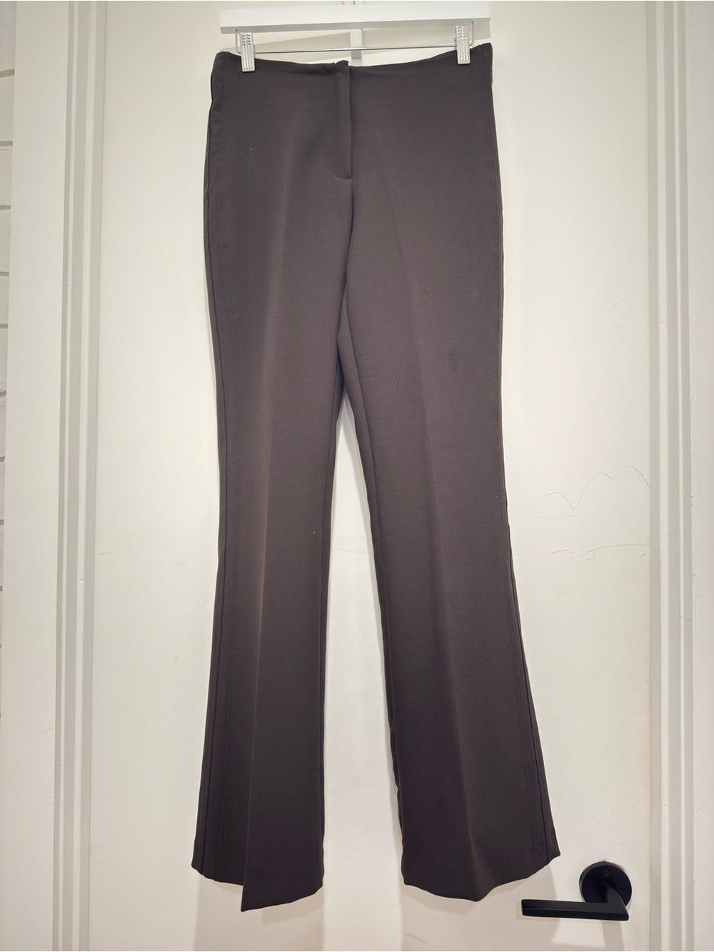 Dark brown pants hanging on a white hanger over a white door.