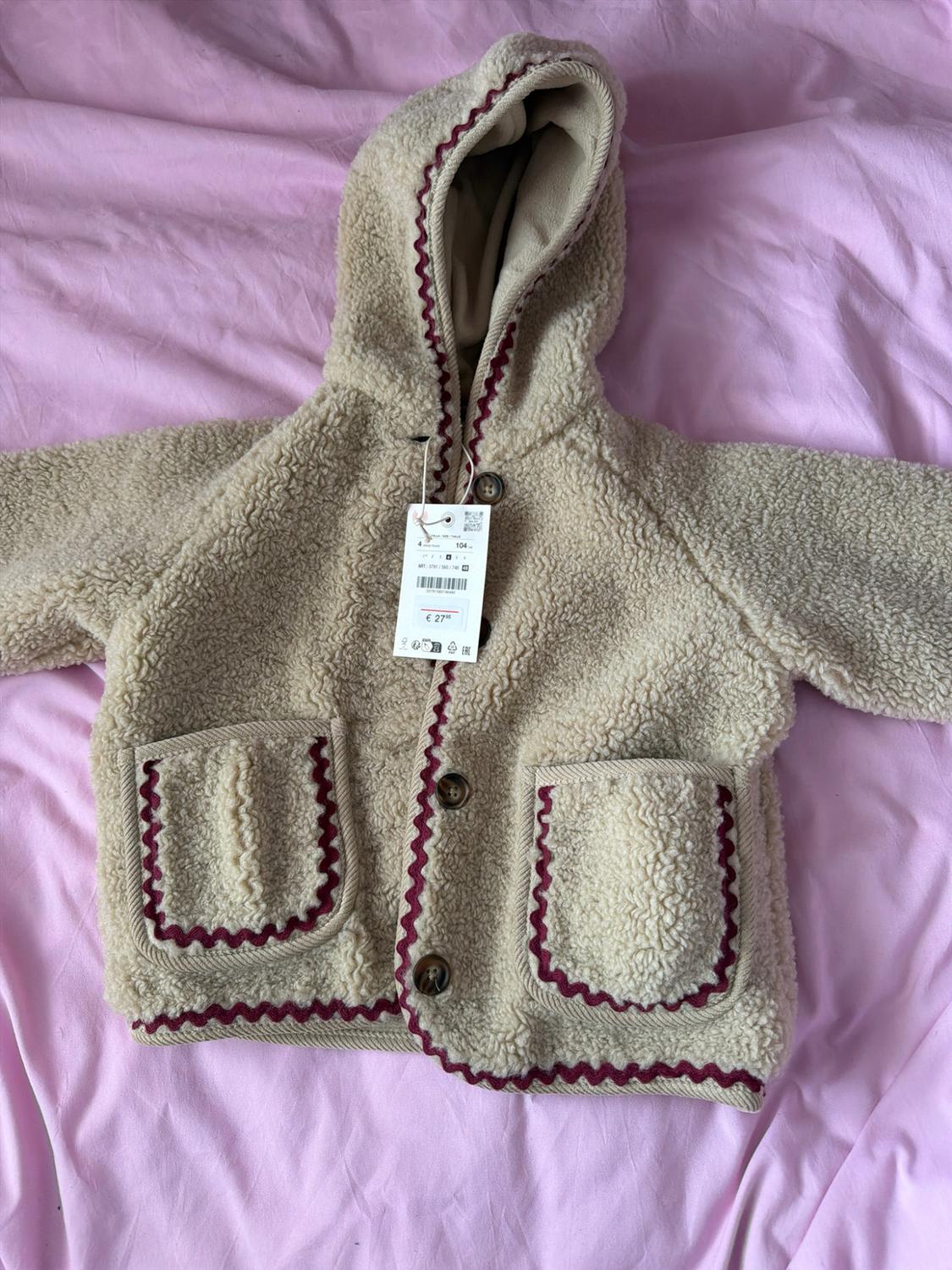 Beige children's fleece jacket with a hood, buttons and scalloped maroon piping on pink fabric. Label with text € 27.95 and 104.