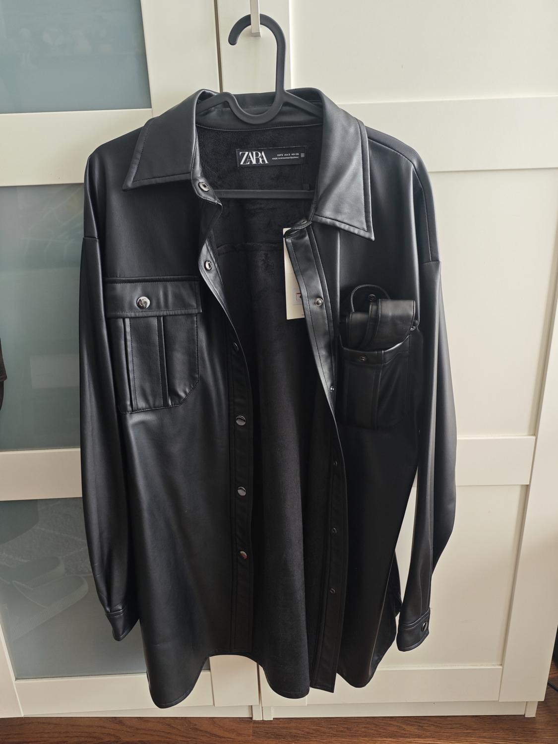 Black synthetic shirt hanging on a hanger, with front pockets and visible ZARA brand label.