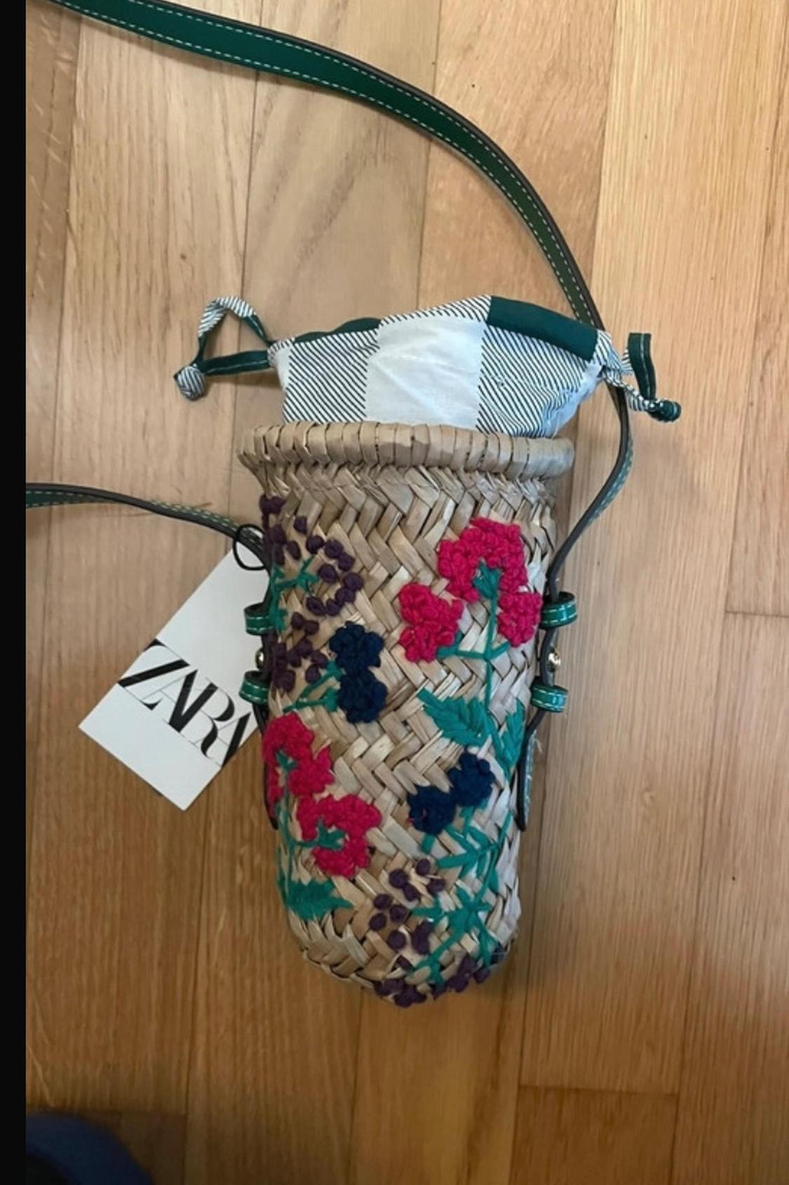 Detail of a woven bag with floral embroidery in pink and blue, drawstring closure and visible label.