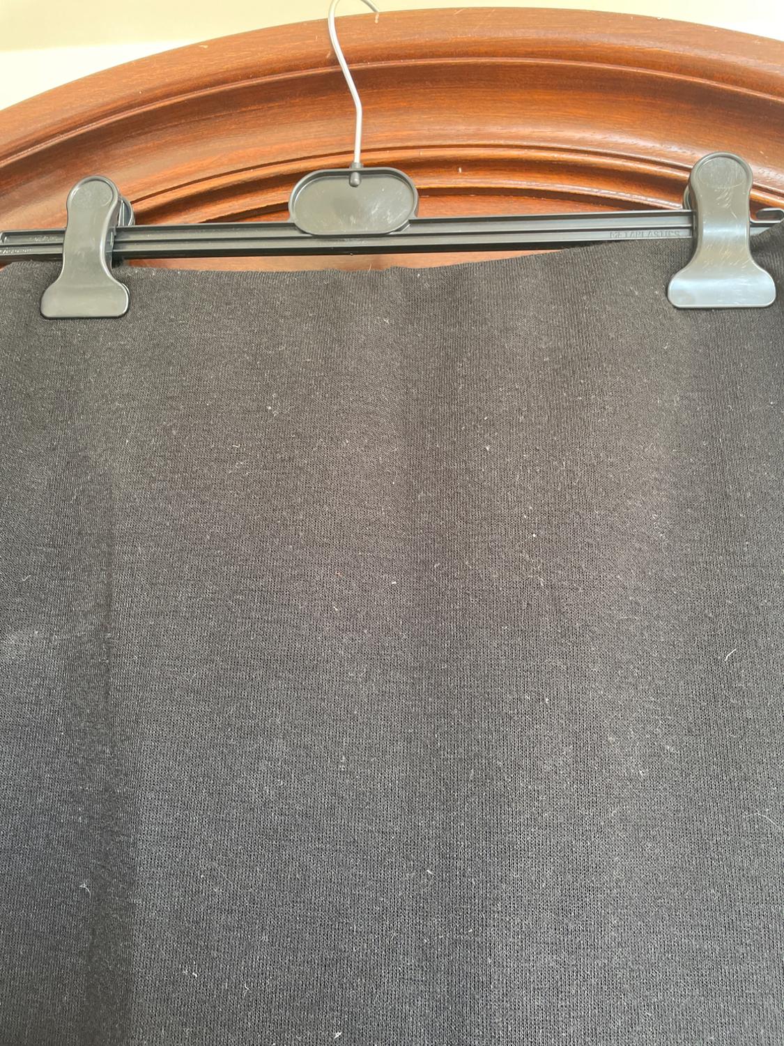 Black plastic coat stand with a dark fabric hanging from it, against a brown wooden background.