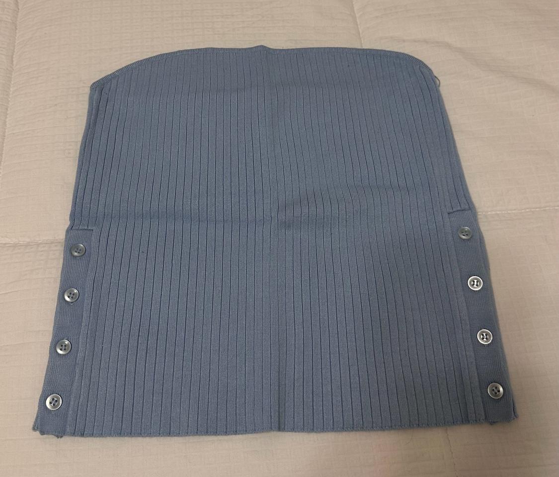 Light blue ribbed knit top with side buttons, laid out on a light-colored bedspread in a casual, relaxed composition.