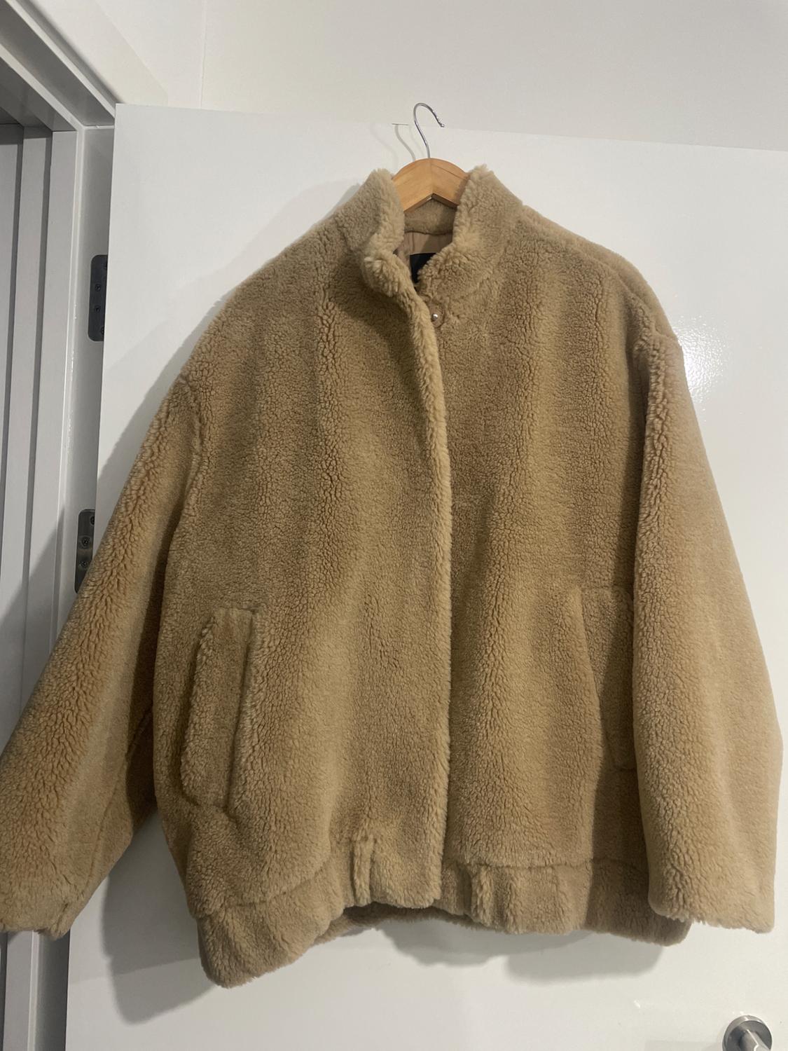 Beige fleece jacket hanging on a wooden coat hanger over a white door. Cosy and casual design.