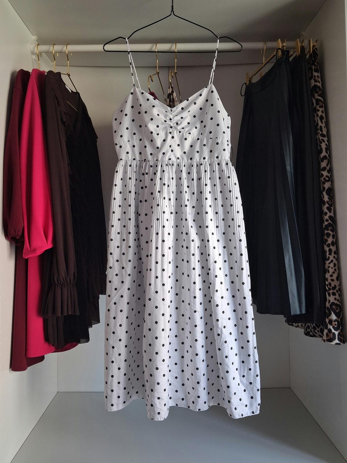 White dress with black polka dots hanging in a wardrobe, surrounded by dark-coloured garments and animal print.