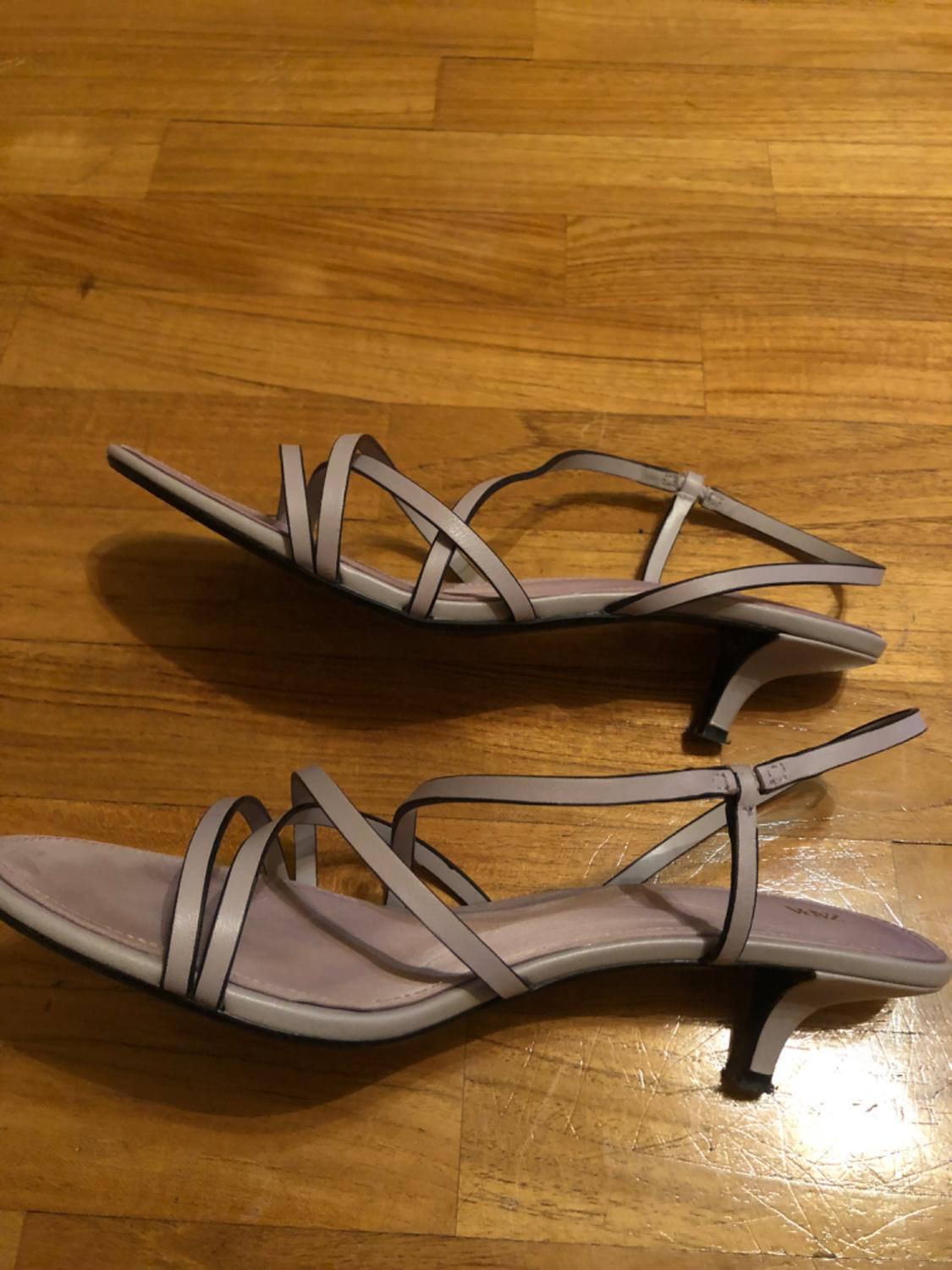Low-heeled sandals with thin straps in a lilac colour, on a wooden floor. Elegant and minimalist design.