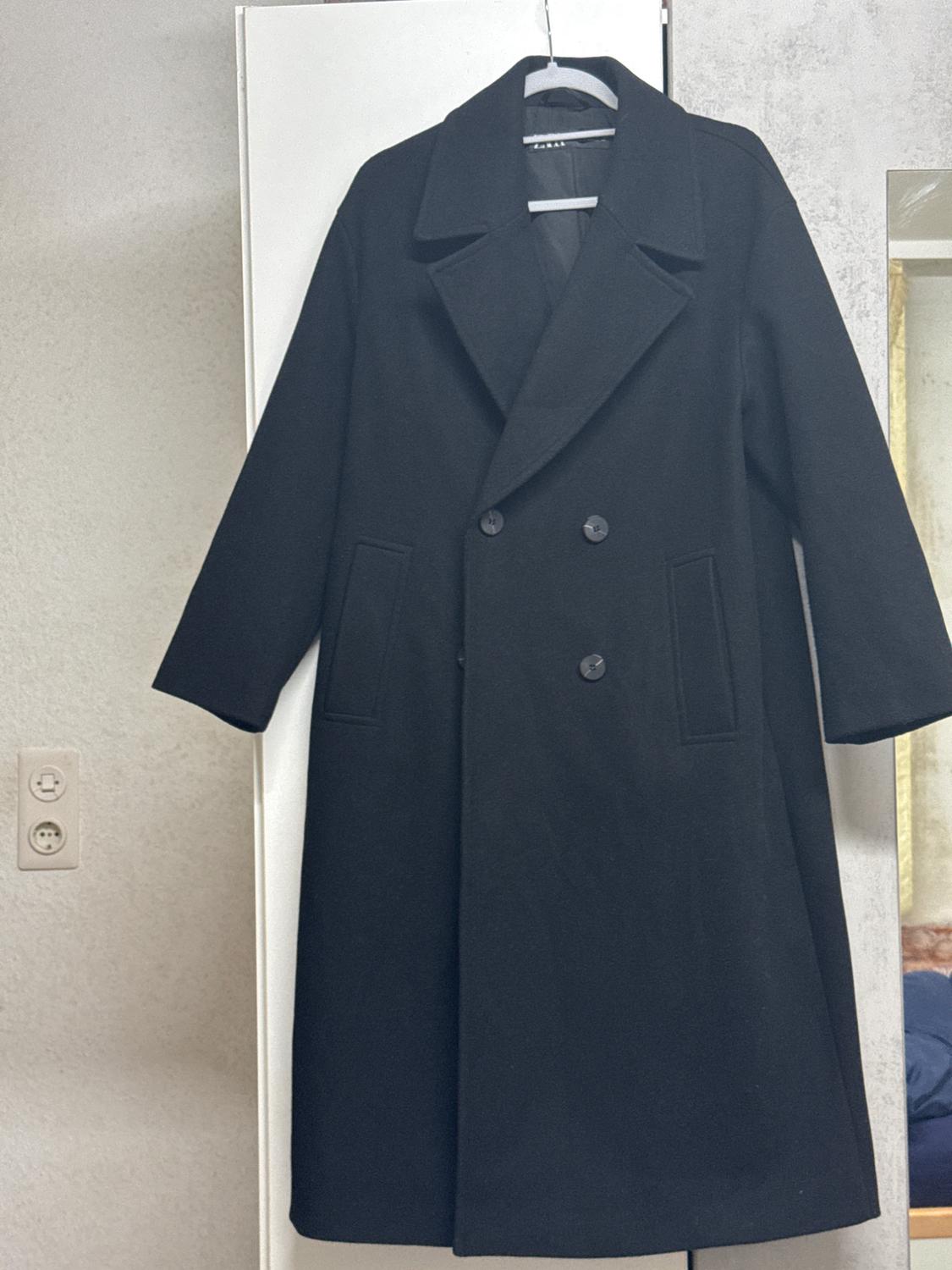 Black wool coat hanging on a hanger over a white door. Classic design with wide lapels and double-breasted buttons.