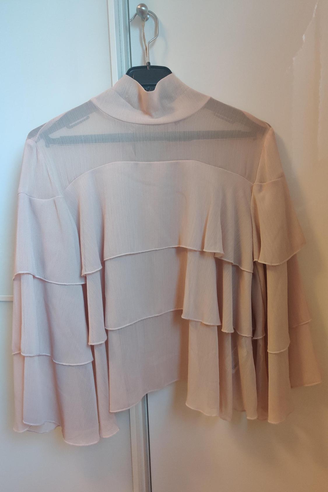 Rear view of beige blouse with tiered frills and high neck.