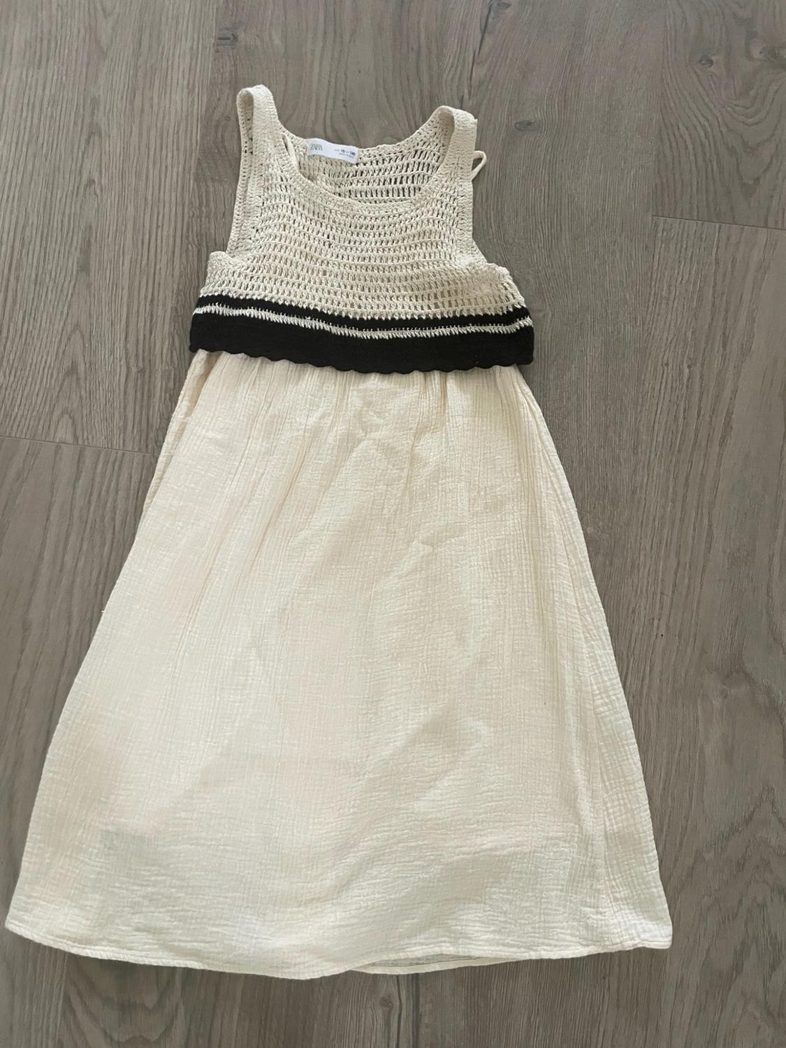 Casual dress laid out on a wooden floor. Beige openwork knit top with a black band and cream-colored crinkled fabric skirt.