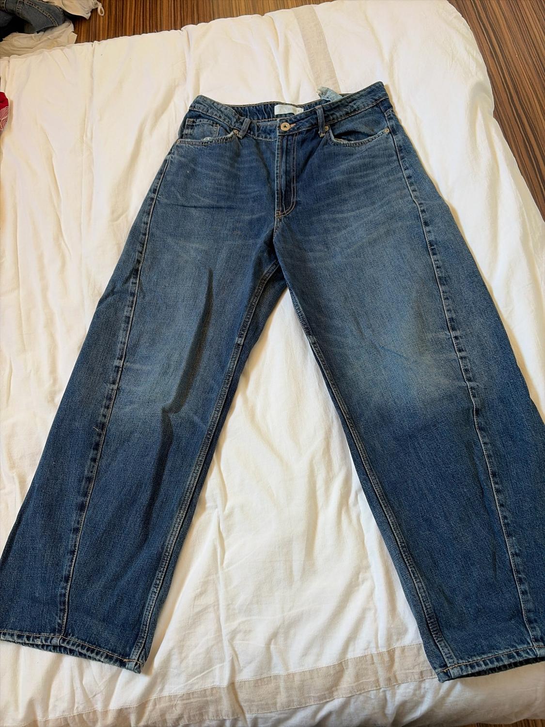 Blue wide-leg jeans with prominent stitching, laid out on a crumpled white sheet.