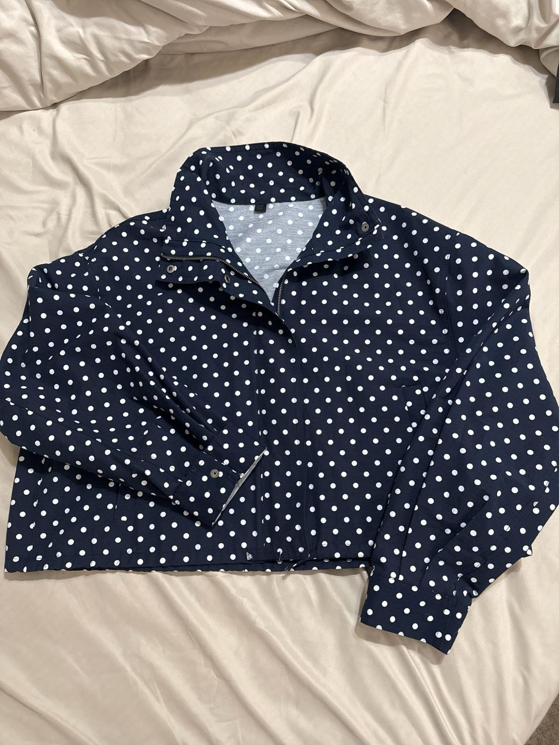 Navy blue jacket with white polka dots and a high collar, laid out on some crumpled pale-coloured bedsheets.