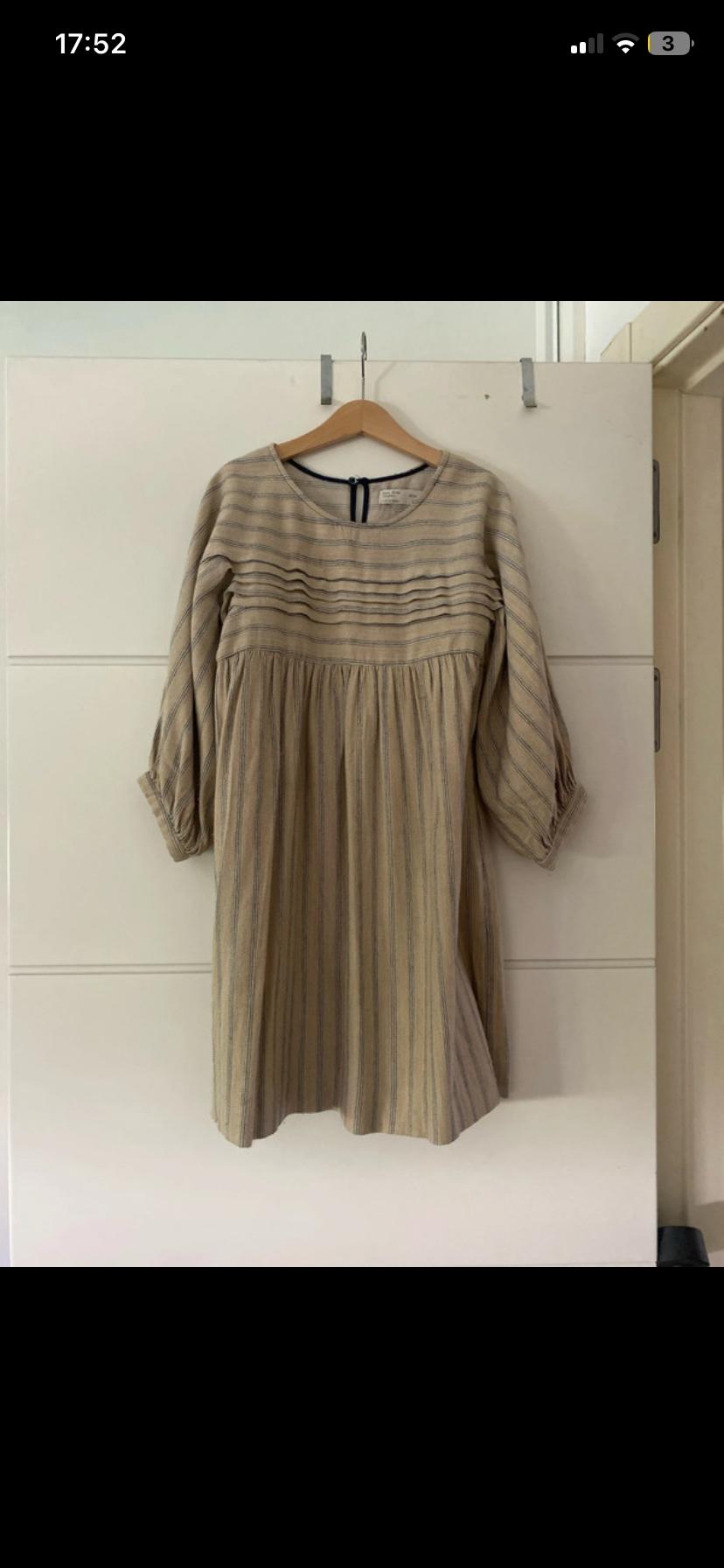 Casual beige striped dress with front pleats and long sleeves, hanging on a hanger on a white door. Text: 17:52 3.