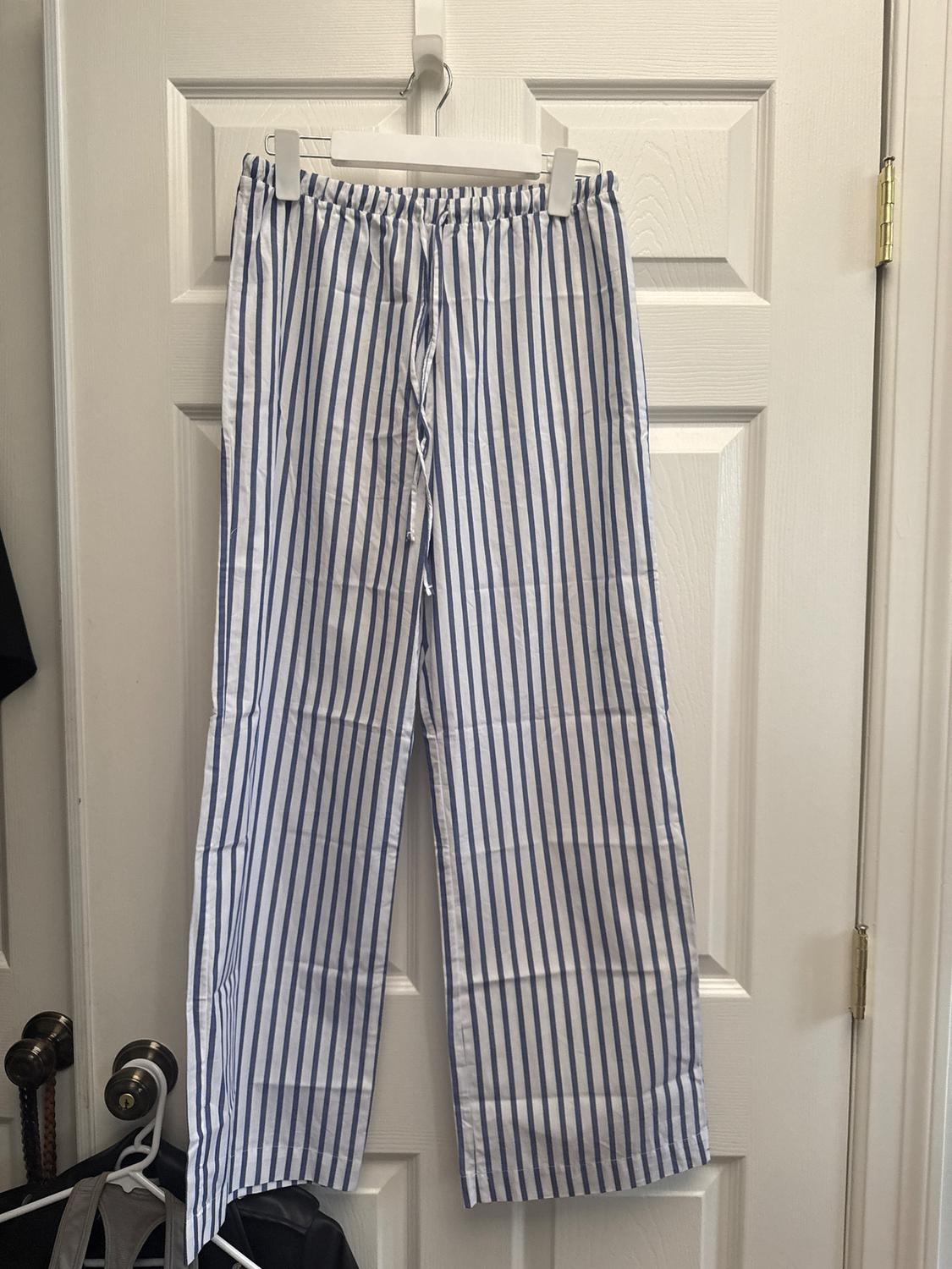 Blue and white vertical striped trousers hanging on a white door with a hanger. Indoor setting.