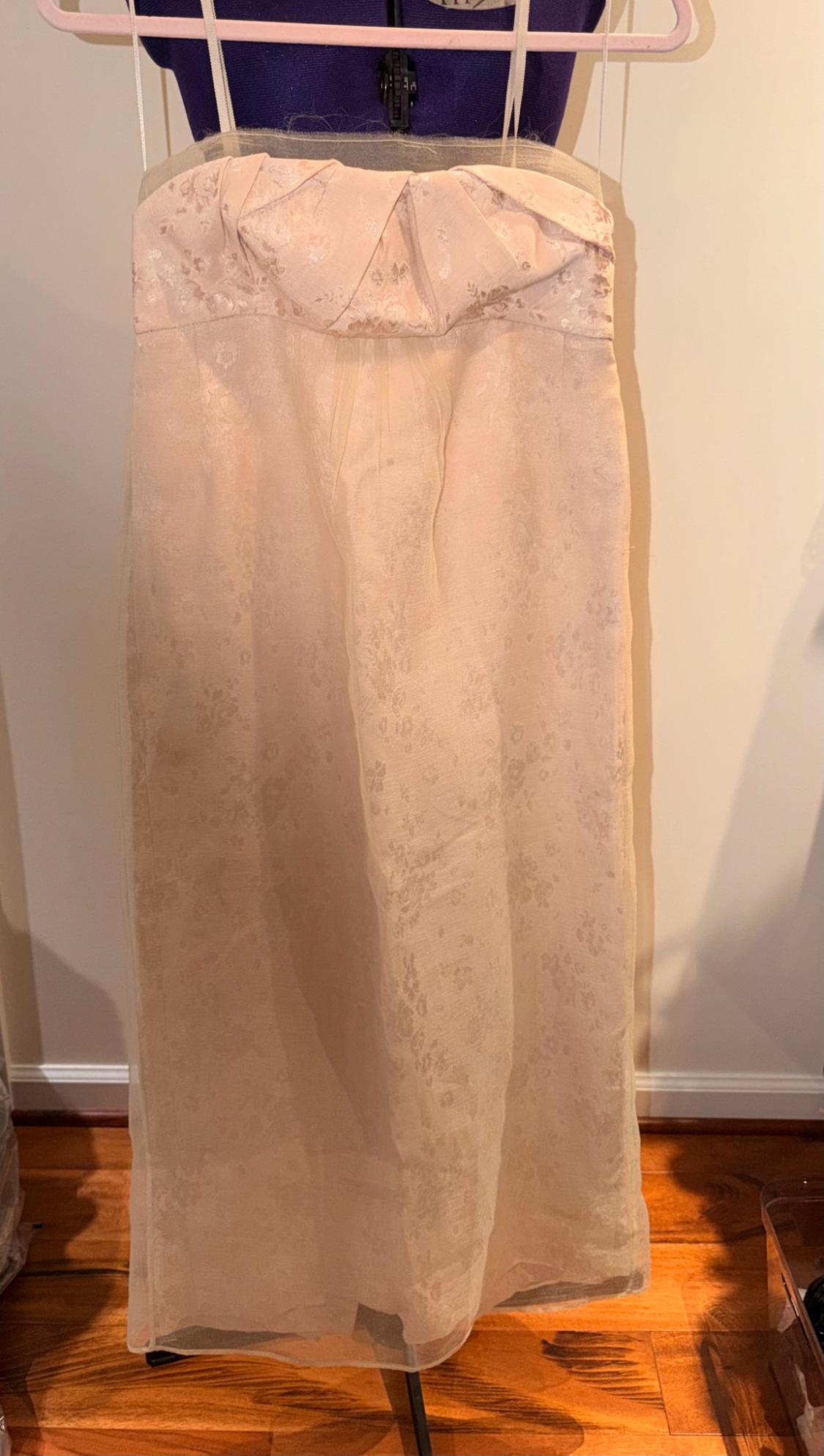 Pale pink strapless maxi dress with a floral print and sheer cape, hanging on a mannequin in front of a white wall.