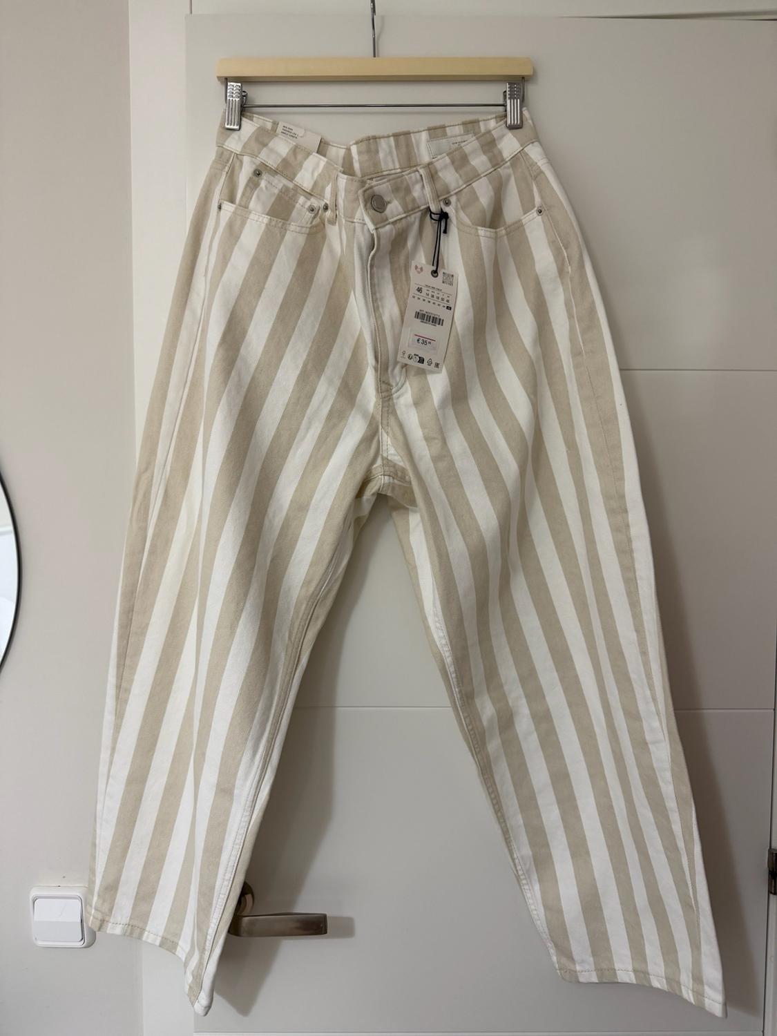 White and beige vertical-striped trousers hanging on a hanger over a white door. Label with the text ZARA and €35.95.