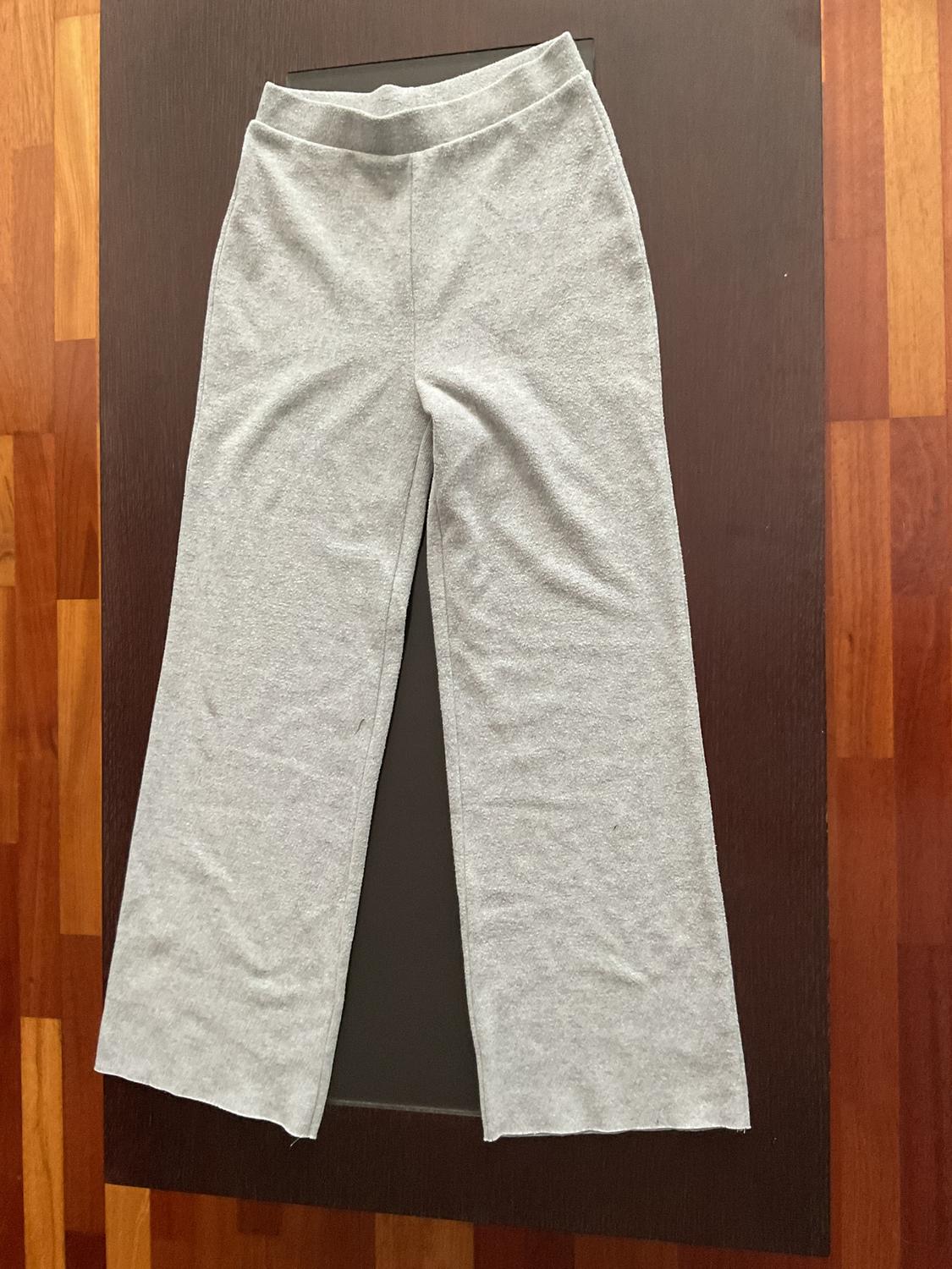 Grey wide-leg trousers on a dark table, with a wooden floor background.