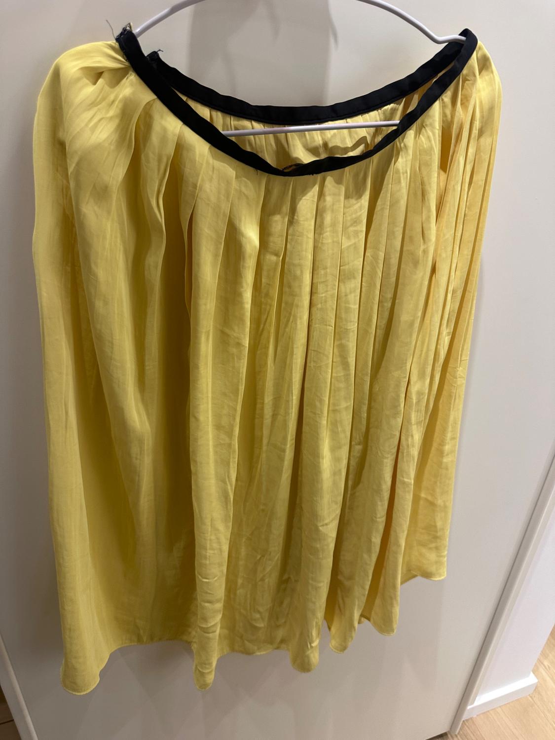 Pleated yellow skirt hanging on a white hanger, with a black trim at the waist, against a white background.