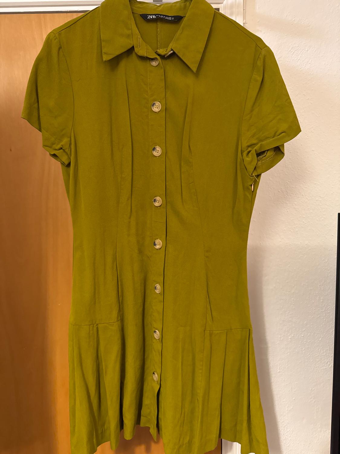 Olive green dress with front buttons and classic collar, hanging on a light wooden door.